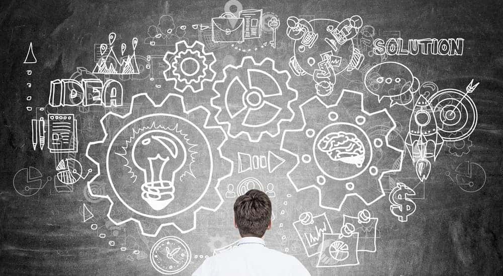 Man in blue shirt looking at chalkboard with gears and words on it