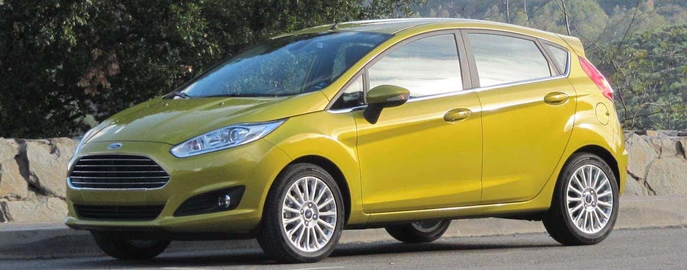 Yellow 2016 Used Ford Fiesta with trees and stone wall in back