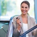 A woman stands inside a dealership with her new car key
