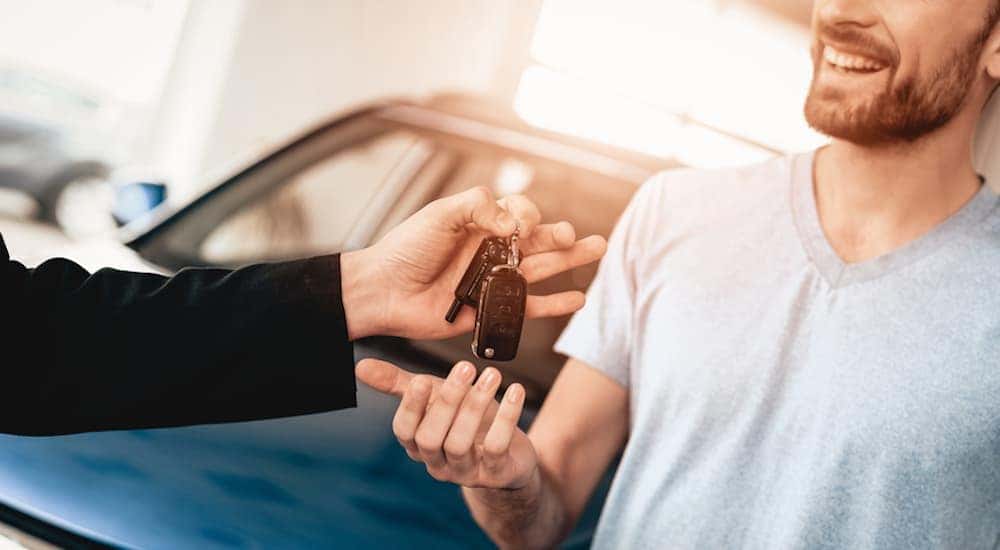 A dealer's hand is giving keys to a smiling man at a Buy Here Pay Here Louisville.