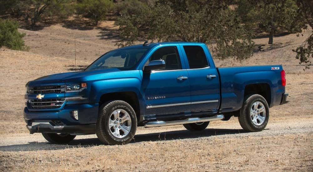 A blue 2016 Chevy Silverado 1500, popular among used trucks for sale in Cincinnati, OH, is on a dirt path.