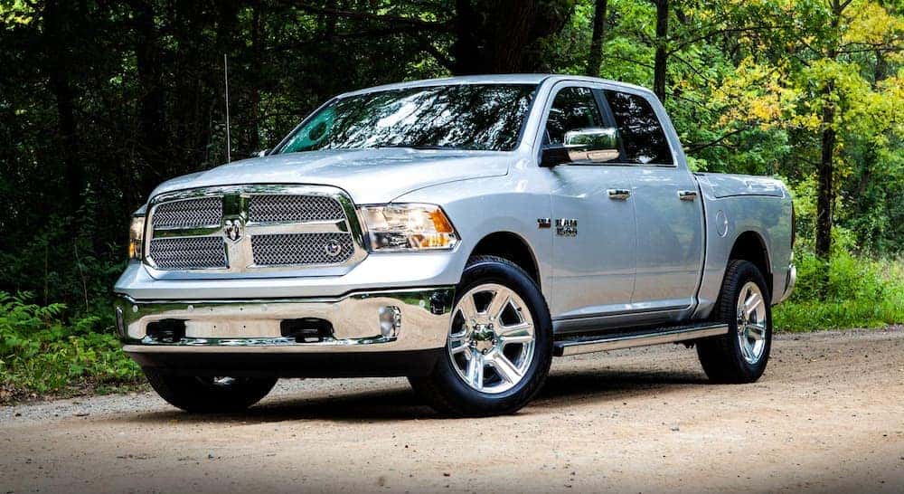 A silver 2018 used Ram 1500 is on a dirt road lined by trees.