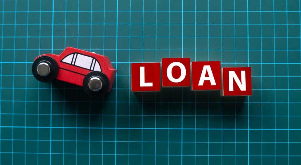 Red, wooden toy car on its side followed by red letter blocks that spell out "LOAN" on a green and blue graph background