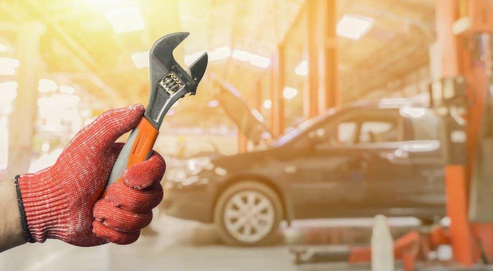 A gloved mechanic is shown holding a wrench in front of a vehicle.