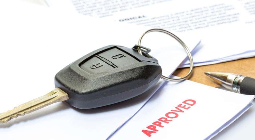 A car key is shown on top of car loan paperwork.