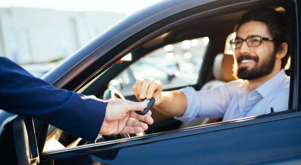 A man is shown handing a car key to a used car salesman.