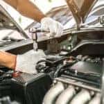 A close up of a mechanic working on a vehicle's engine is shown.
