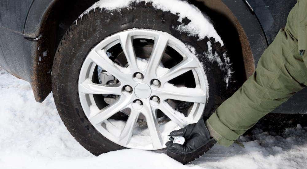 A closeup shows a gloved hand checking the tire pressure on a snow-covered tire as part of a winter car service near you.