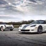 A white 1953 Corvette is parked next to a 2013 Chevy Corvette 427 60th Anniversary Edition on a cloudy day.