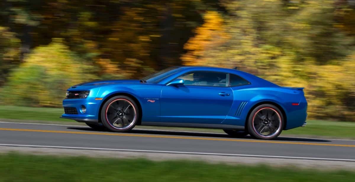 A blue Chevy Camaro driving on a wooded road
