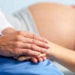 Hand of assistant or nurse holding that of pregnant female
