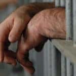mans hands behind bars in jail or prison