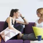 Two happy young female friends conversing in the living room at home