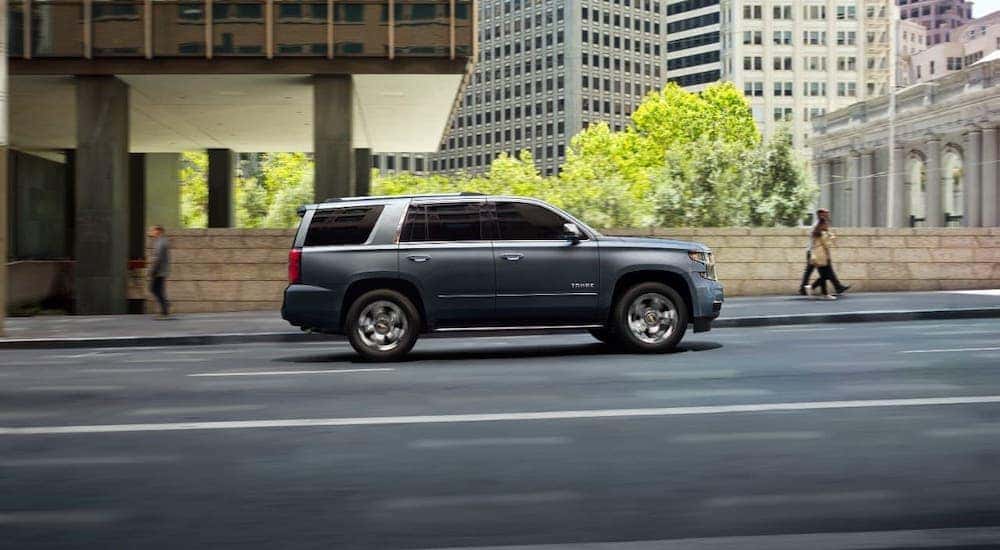 A gray 2020 Chevy Tahoe is shown from the side driving on a city street after leaving a Cincinnati used car dealership.