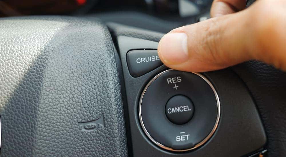 A thumb is shown pushing the cruise button on a steering wheel.