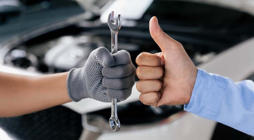 Mechanic holding a spanner while another is showing a thumbs up.