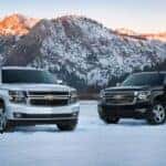 White 2015 Chevy Tahoe and a black 2015 Chevy Suburban parked by a lake.