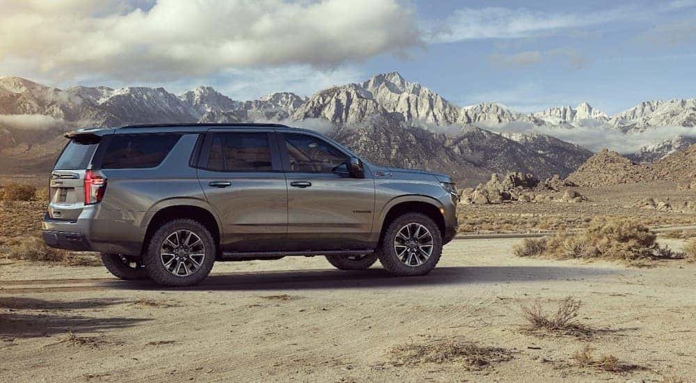 A dark gray 2021 Chevy Tahoe is parked in front of mountains and a cloudy blue sky.
