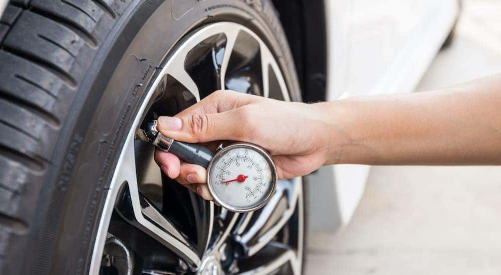 A hand is holding a tire gage to check the tire pressure on a car.