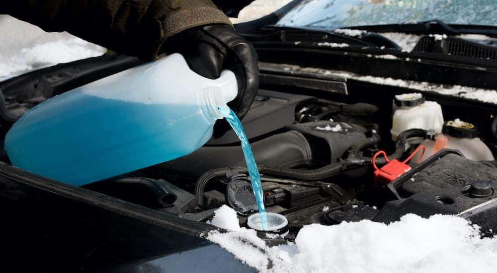 A person is adding coolant to a car in the wintertime.