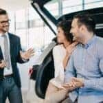 A salesman is shown speaking to a couple at a used car dealership in Cincinnati.