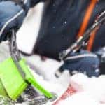 A closeup shows someone using a green snow brush to clean off a red car at a Chevy dealer in Ohio.