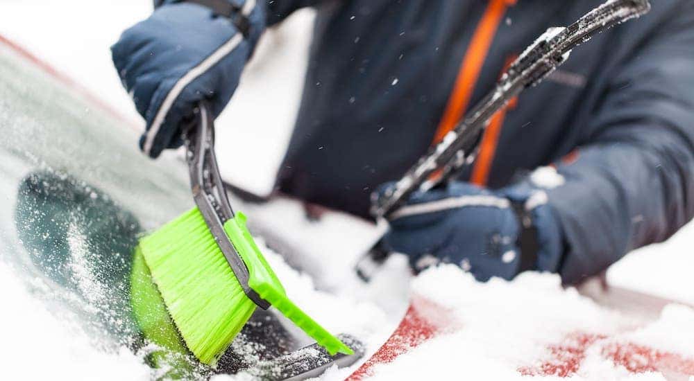 A closeup shows someone using a green snow brush to clean off a red car at a Chevy dealer in Ohio.