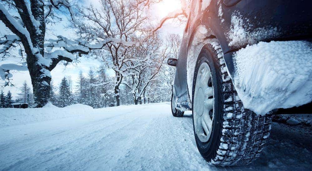 A closeup shows a tire and car driving on a snowy road in Ohio.
