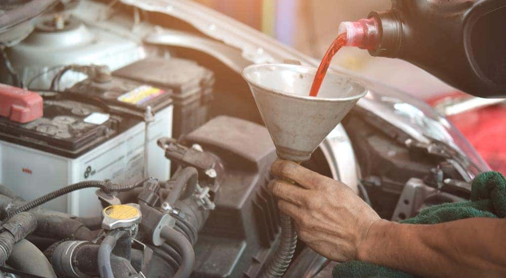 Hands are pouring transmission fluid into a funnel as part of an auto repair in Cincinnati.