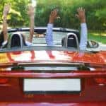 Happy free couple driving in red retro car cheering joyful with arms raised