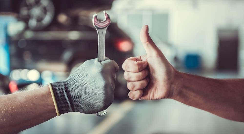 A mechanic is holding a wrench and giving a thumbs up.