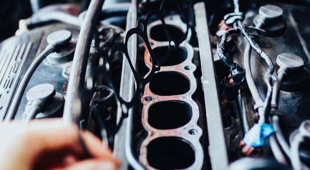 A hand is holding a manifold gasket over an engine.