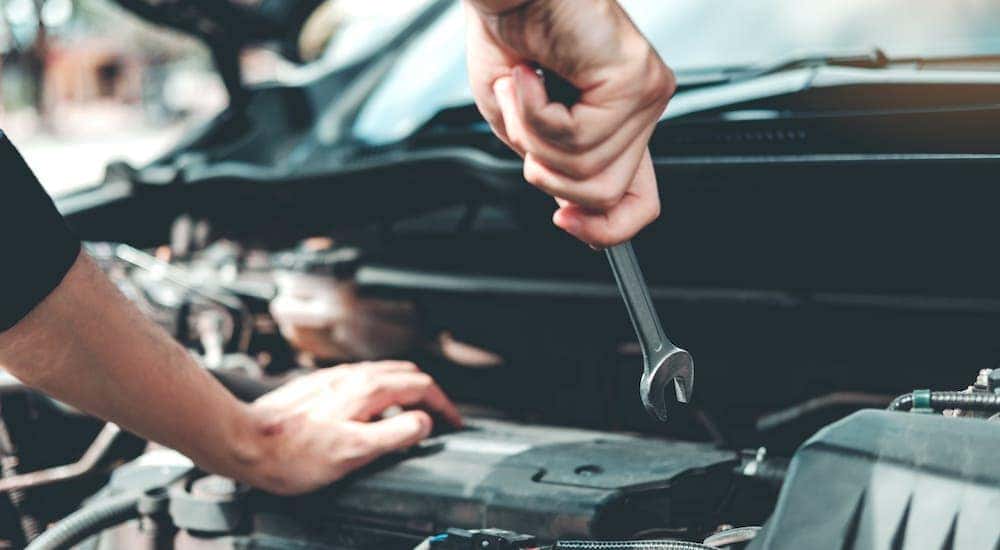 A mechanic is holding a wrench over an engine bay.