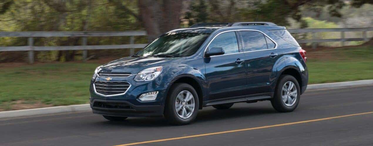 A blue 2016 Chevy Equinox driving near a fence.