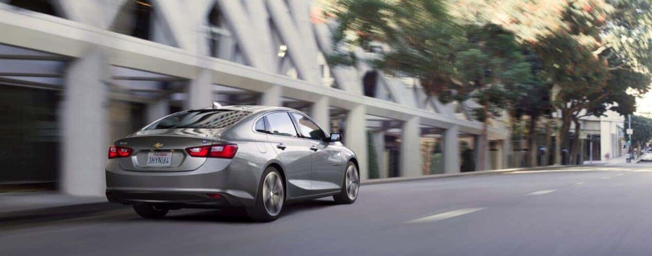A silver 2016 Chevy Malibu driving in a city.