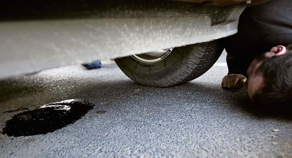 A man is shown looking at an oil spill under a vehicle.