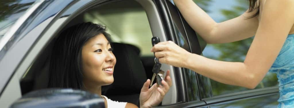A woman handing car keys to a woman inside a car