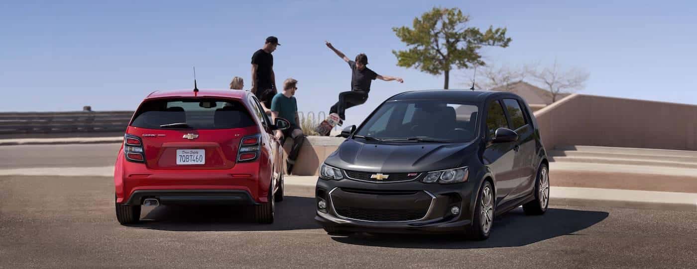 A red and a gray 2017 Chevy Sonic Hatchbacks are at a skatepark in front of skateboarders.
