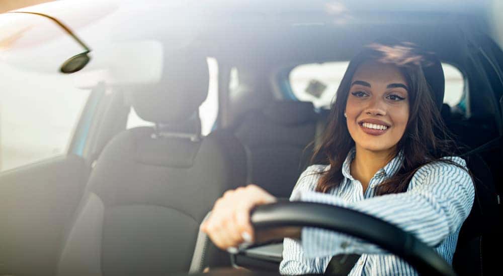 A woman in a blue and white button-up is shown driving a car.