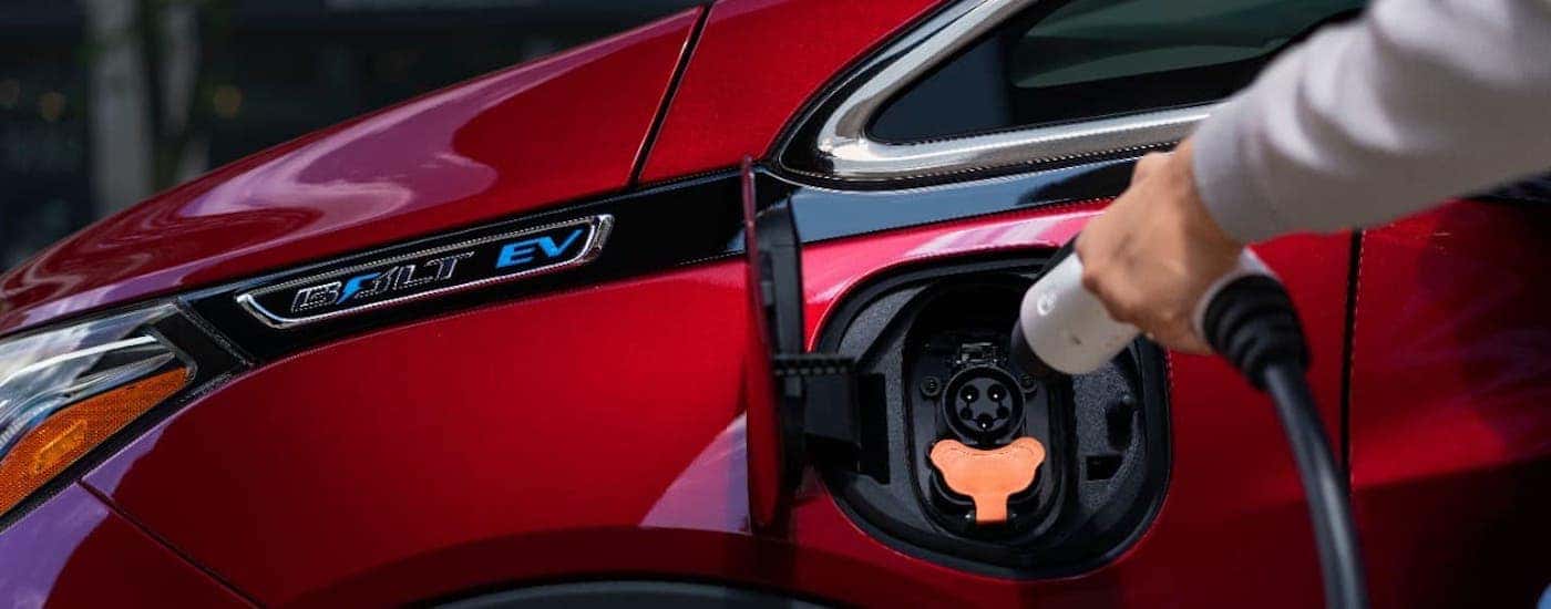 A closeup shows a hand plugging in a red 2020 Chevy Bolt EV at a Chevy dealer in Ohio.