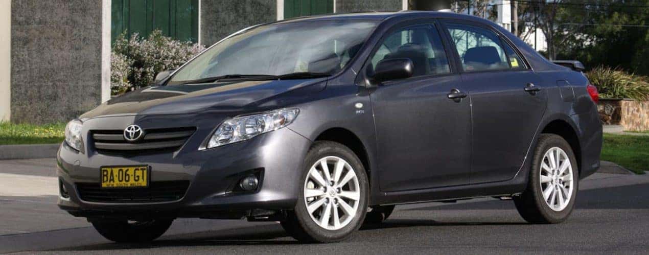 A gray 2010 Used Toyota Corolla is shown in front of glass building.