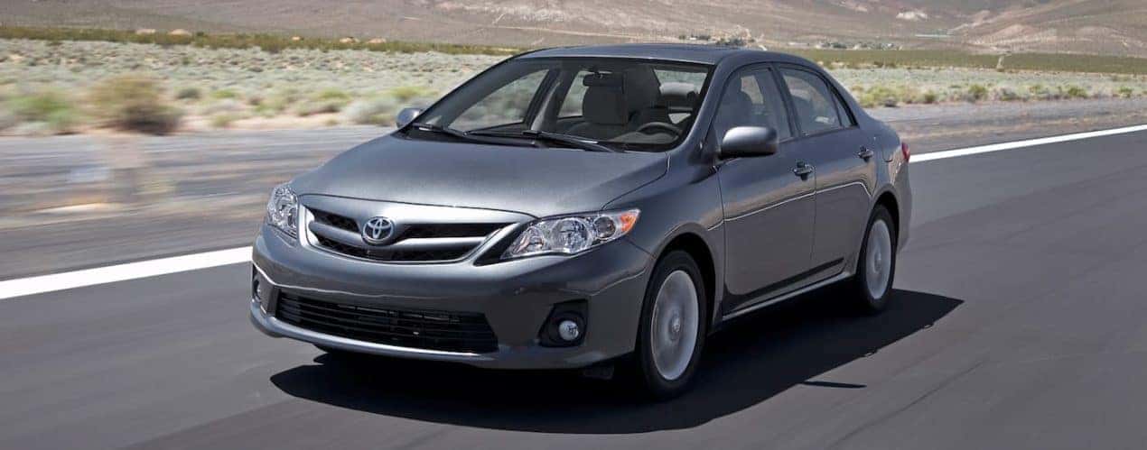 A grey 2011 used Toyota Corolla is shown driving past distant mountains.