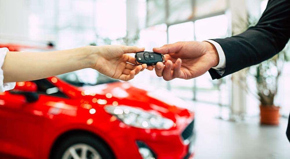 Car keys are being handed over in a car dealership in front of a red car.