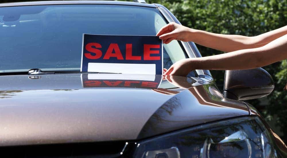 A sign that reads "SALE" is being placed on a copper-colored sedan.
