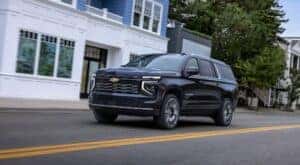 A black 2025 Chevy Suburban High Country is shown driving through a town.