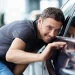A man inspects a new car with his head close to the window