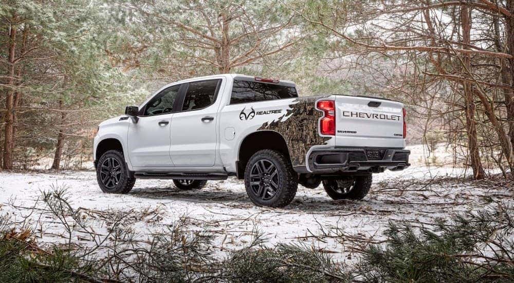 A white 2021 Chevy Silverado 1500 Realtree is shown from the rear parked in the woods.