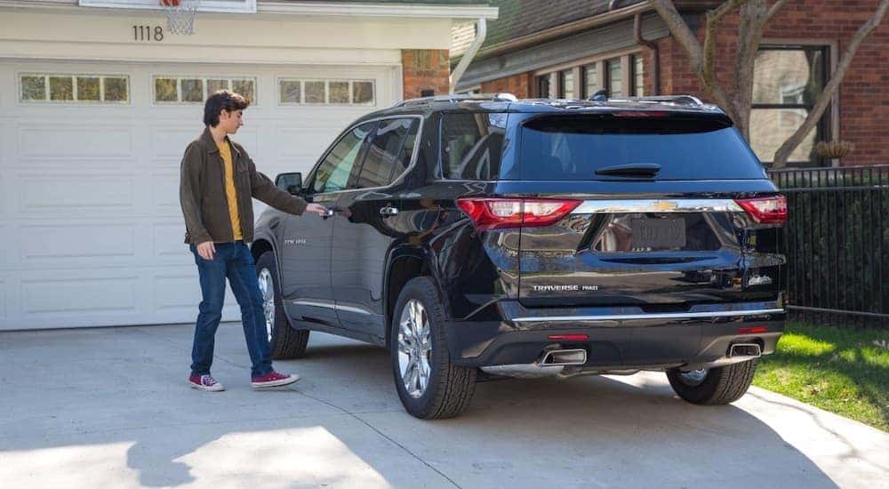 A teen boy is reaching for the door on a blue 2019 Chevy Traverse in a driveway after leaving a Chevy dealer in Ohio.