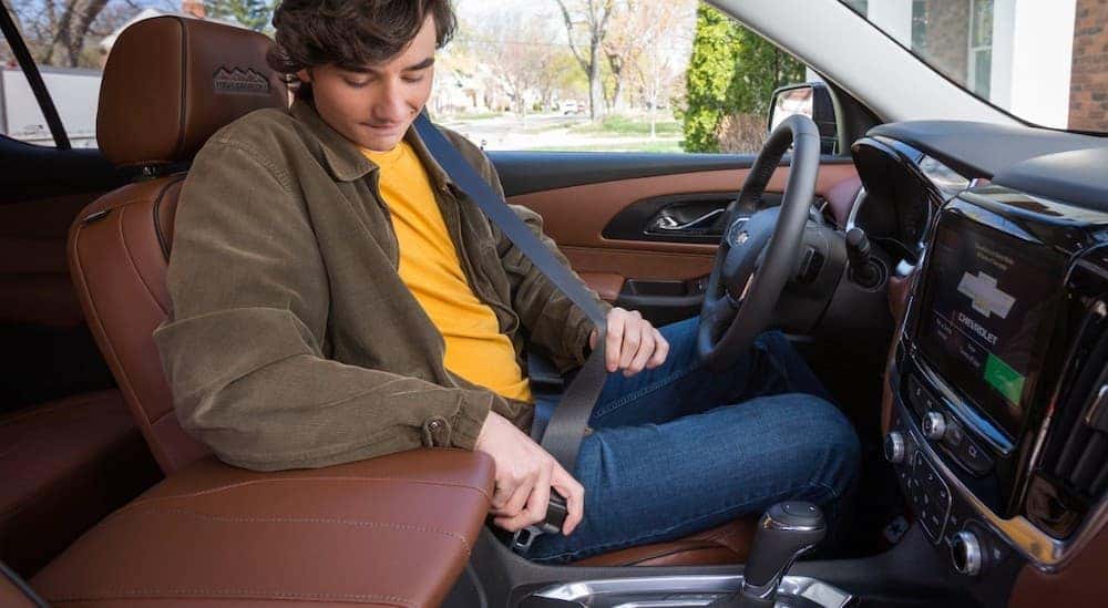 A teen boy is buckling his seatbelt inside a 2019 Chevy Traverse.