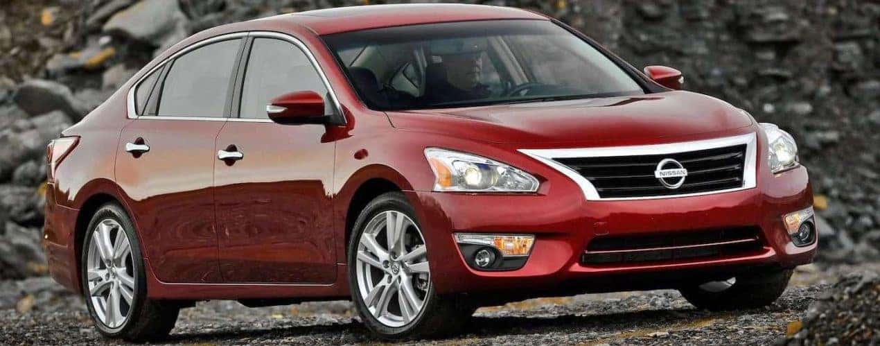 A red 2013 used Nissan Altima is parked in a gravel pit.